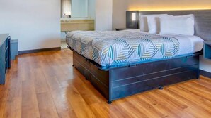 Un dormitorio con cama, mesita de noche, espejo y suelo de madera.