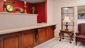 Un área de recepción con mostrador de madera, pared roja, un reloj y una lámpara.