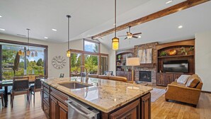 A spacious kitchen with a large island, wooden cabinets, and a built-in oven. There is a dining area with a table and chairs, and a cozy living room with a fireplace and a flat-screen TV. - Cozy Caldera Cabin with Access to Forest House (Bend)
