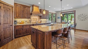 A spacious kitchen with wooden cabinets, a large island with bar stools, and a built-in oven. - Cozy Caldera Cabin with Access to Forest House (Bend)