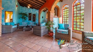 Amplia zona de patio con mobiliario de mimbre, piso de baldosas y ventanas grandes con arcos.