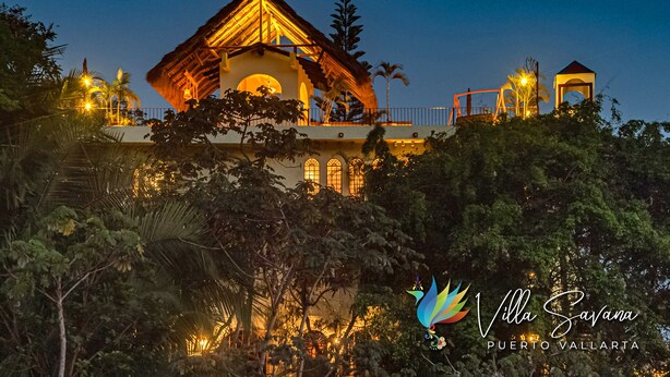 Una villa con techo de paja, varios balcones e iluminación exterior.