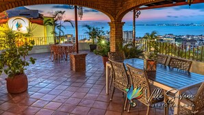 Un patio con una mesa y sillas, plantas en macetas y vistas al mar y al paisaje urbano.