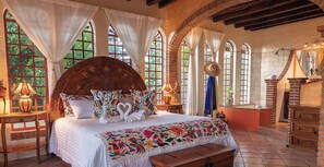 A bedroom with a large bed, multiple windows, and a wooden chest of drawers.