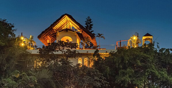 A villa with a thatched roof, multiple balconies, and a well-lit facade.