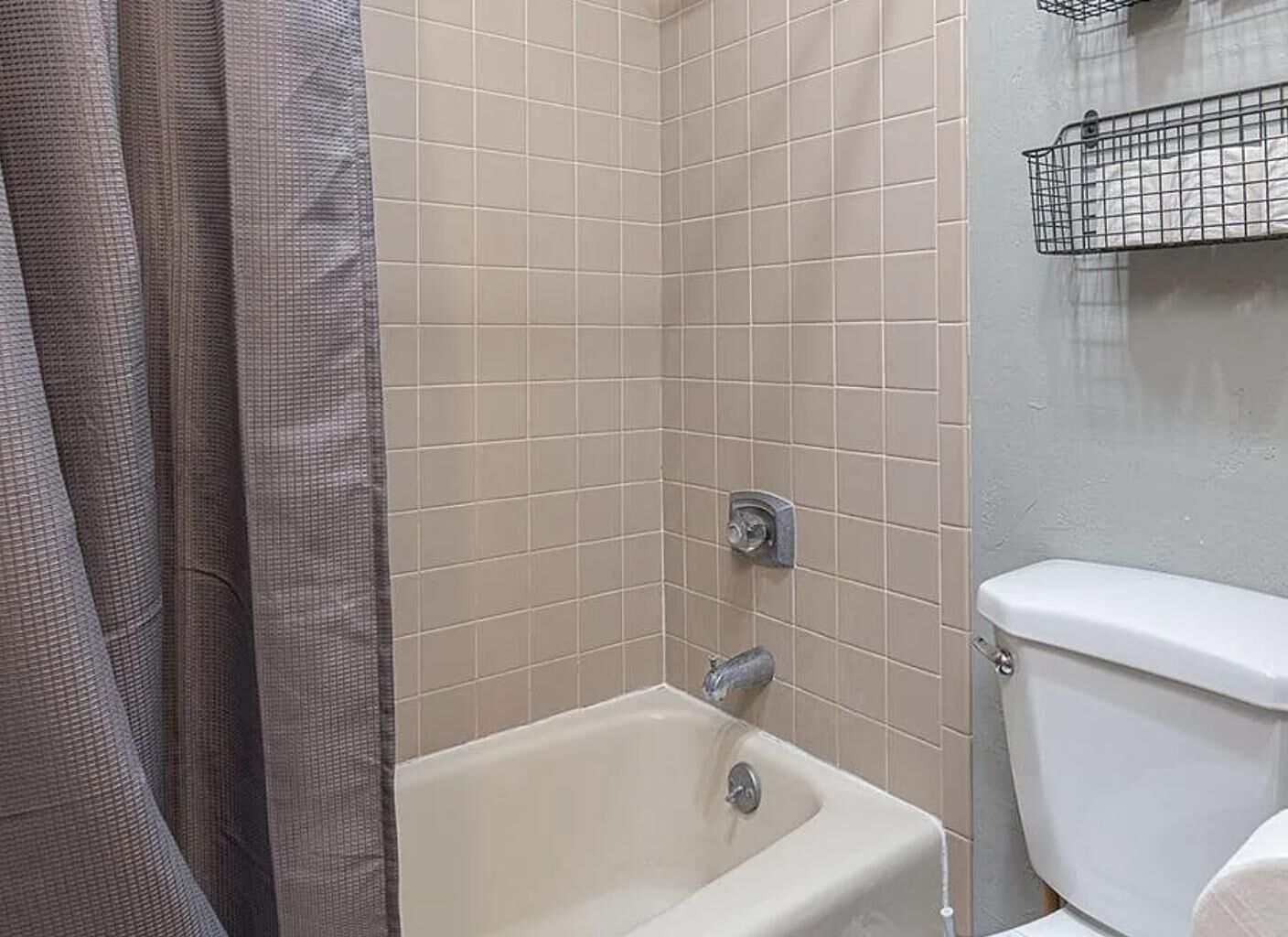 Et badeværelse med beige fliser, et badekar, et toilet og en metalkasse.