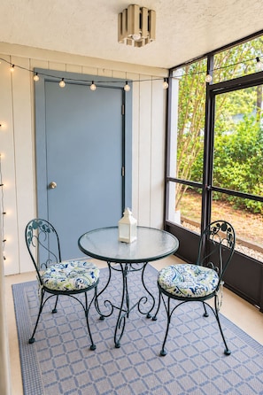 Une pièce avec une table ronde en verre, deux chaises dotées de coussins à motifs, une lanterne blanche et des guirlandes lumineuses.