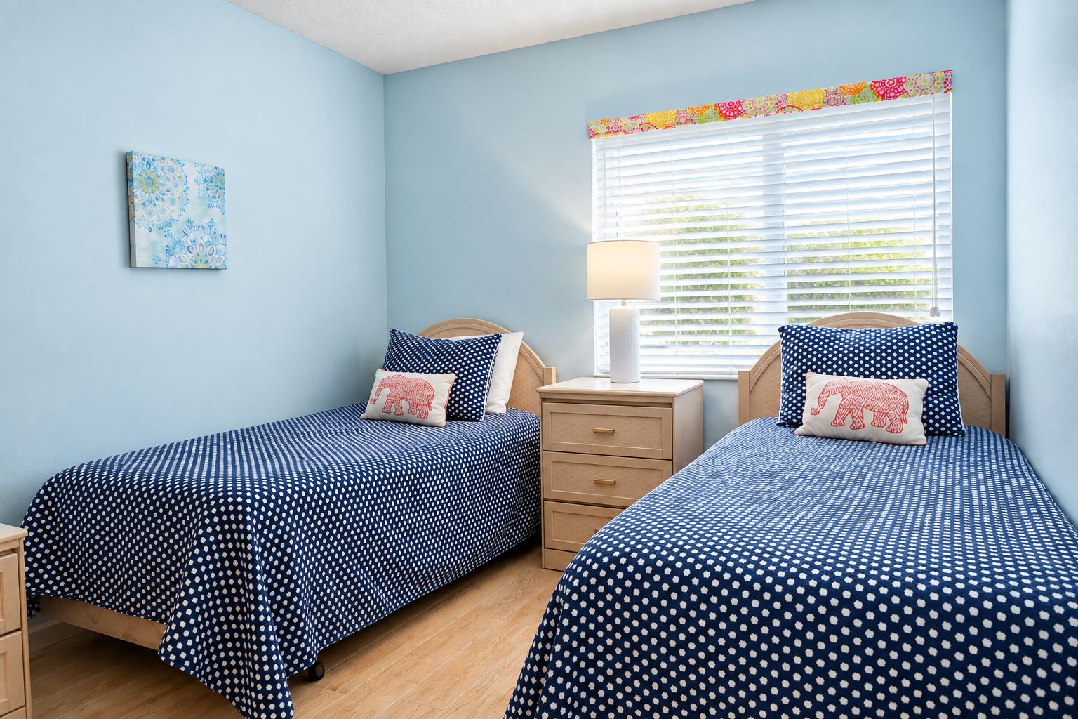 A bedroom with two single beds, a nightstand, a lamp, and a window with blinds.