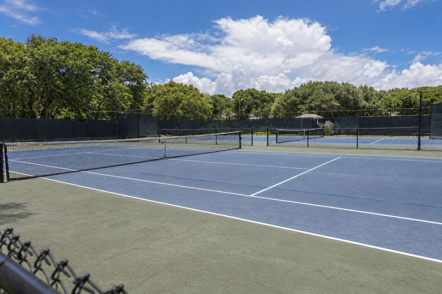 A tennis court with a net, surrounded by trees and a clear sky.