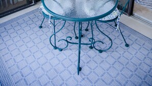 Een glazen tafel met een witte lantaarn, omringd door metalen stoelen met bloemmotieven, op een vloer met een patroon.