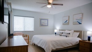 Een slaapkamer met een bed, nachtkastjes, een bureau, een stoel, een plafondventilator en kunstwerken aan de muren.