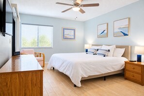 A bedroom with a bed, bedside tables, a desk, a chair, a ceiling fan, and artwork on the walls.