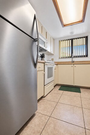Una cocina con un refrigerador de acero inoxidable, un microondas, un horno y una ventana con persianas verticales.