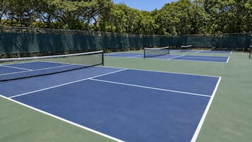 Una cancha de tenis con una red, rodeada de árboles y una cerca.