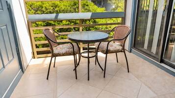 Un balcón con una mesa y sillas, vista a un edificio y una puerta.