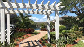 A pathway leading through a garden with a pergola structure. - 250 Sea Woods - 3BD - Your Beach Escape Awaits (New Smyrna Beach)