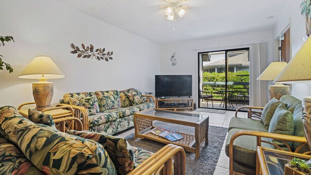 A living room with a sofa, armchairs, a coffee table, and a TV. There is a window with a view of greenery outside. - 250 Sea Woods - 3BD - Your Beach Escape Awaits (New Smyrna Beach)