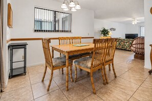 A dining area with a wooden table and chairs, a small side table, and a window with bars.