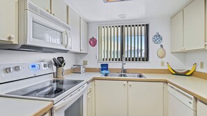 A kitchen with white cabinets, a microwave, stove, and a sink. - 250 Sea Woods - 3BD - Your Beach Escape Awaits (New Smyrna Beach)