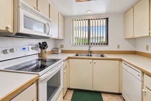A compact kitchen with a stove, microwave, and sink. - 250 Sea Woods - 3BD - Your Beach Escape Awaits (New Smyrna Beach)
