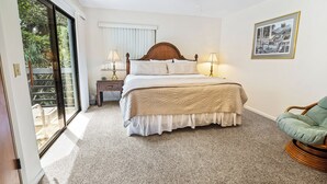A bedroom with a large bed, two bedside lamps, a ceiling fan, and a view through a sliding glass door.