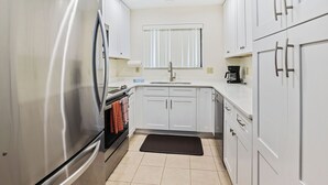 A modern kitchen with white cabinets, stainless steel appliances, and a black mat on the floor.
