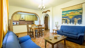 Una sala de estar con un sofá azul, una mesa de comedor con sillas y una zona de cocina con armarios de madera y un salpicadero de ladrillo.