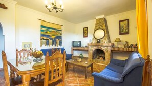 Un salón acogedor con chimenea de piedra, una mesa de comedor con sillas, un sofá azul y una araña.