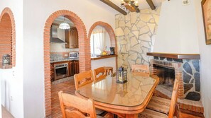 A dining area with a glass table, wooden chairs, and a brick fireplace. - Casa Vistamar Torrox by Ruralidays (Málaga)