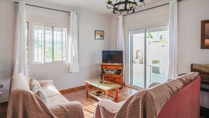 Ein Wohnzimmer mit einer Couch, einem Couchtisch, einem Fernseher und einer Glastür zum Außenbereich.