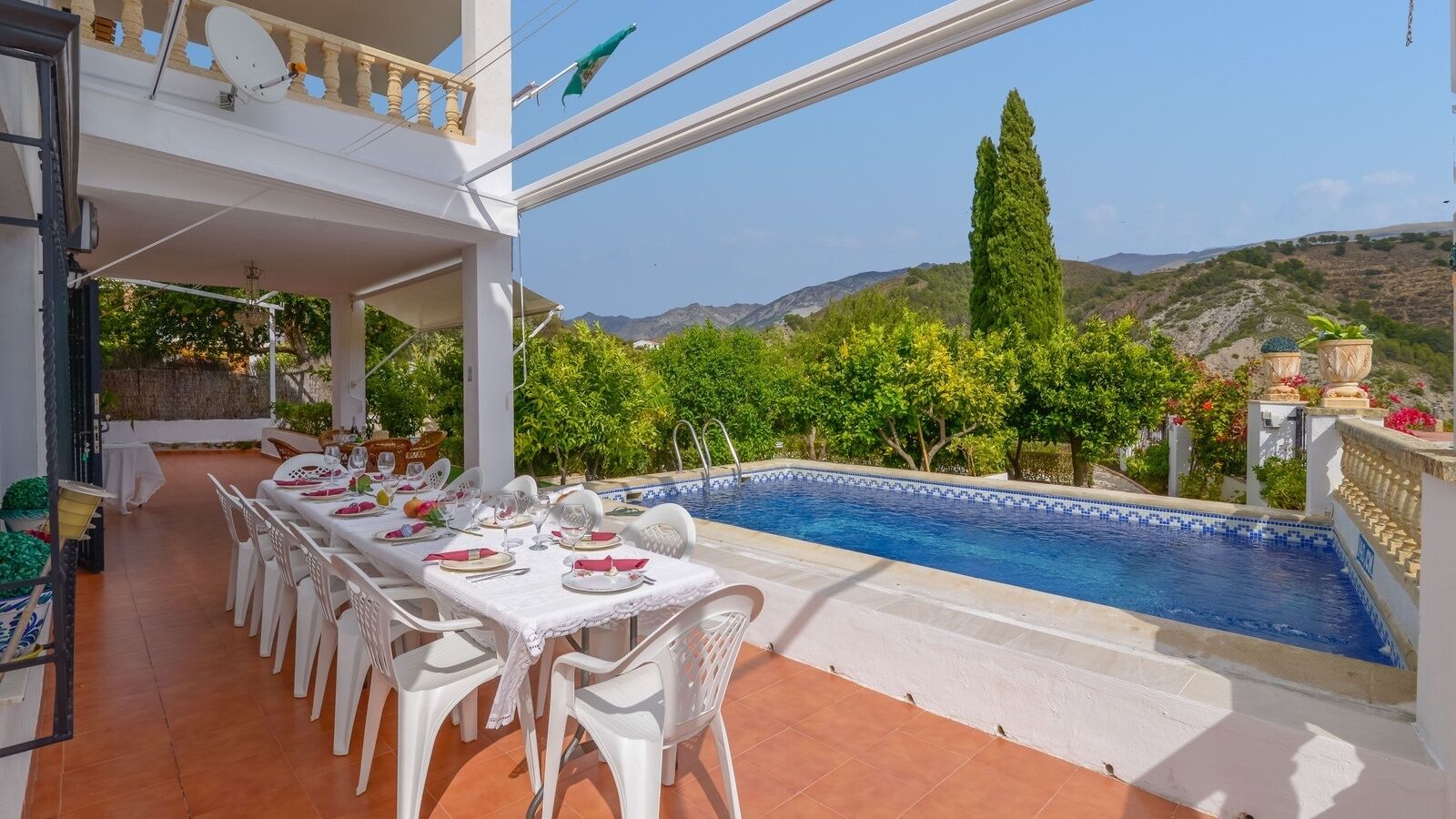 A dining area with a pool view, white chairs, and a table set for a meal.