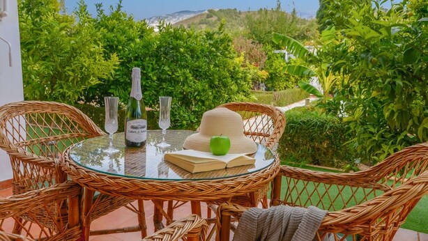 A round glass table with wicker chairs, a bottle of wine, two glasses, a hat, and a book. - Casa Rural Parador del Silo Cónchar by Ruralidays (Granada)