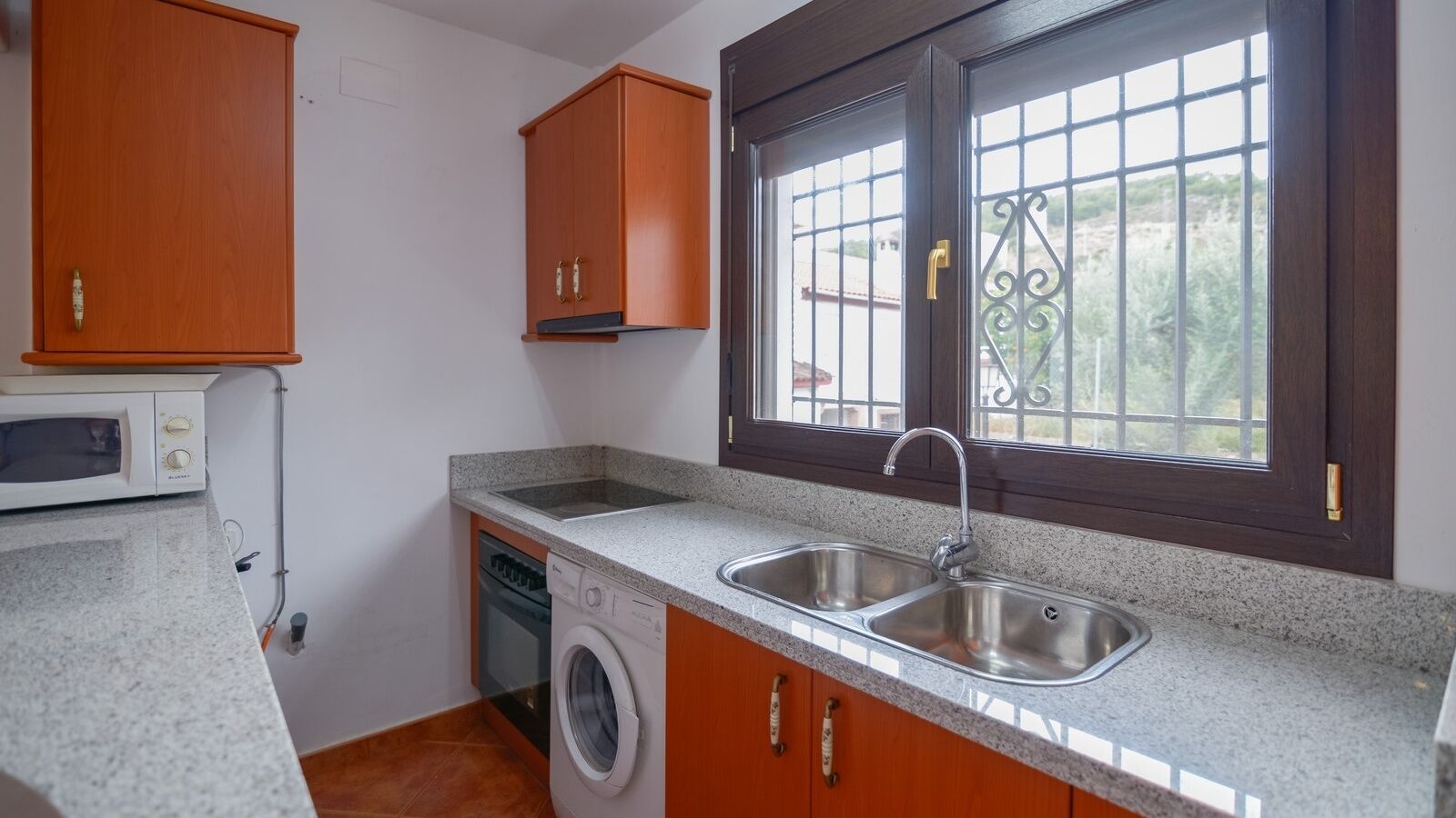 A compact kitchen with a washing machine, a microwave, and a double sink.