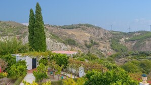 A hillside property with a small building, a tall cypress tree, and wind turbines in the background. - Casa Rural Parador del Silo Cónchar by Ruralidays (Granada)