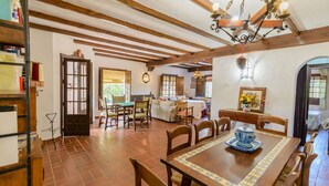 A spacious dining area with a wooden table and chairs, a kitchen in the background, and a rustic ceiling with exposed beams. - Casa El Rosario Ronda by Ruralidays (Málaga)