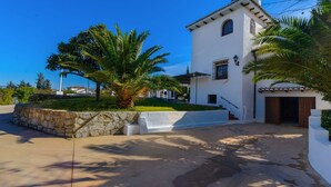 A white building with a stone retaining wall, palm trees, and a clear blue sky. - Casa El Rosario Ronda by Ruralidays (Málaga)