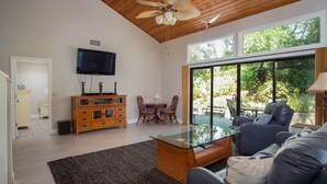 A modern living room with a glass coffee table, leather sofa, wooden cabinet, and a ceiling fan. - 4305 Sea Woods Home 3/3.5 - Stay Salty, Sleep Happy (New Smyrna Beach)