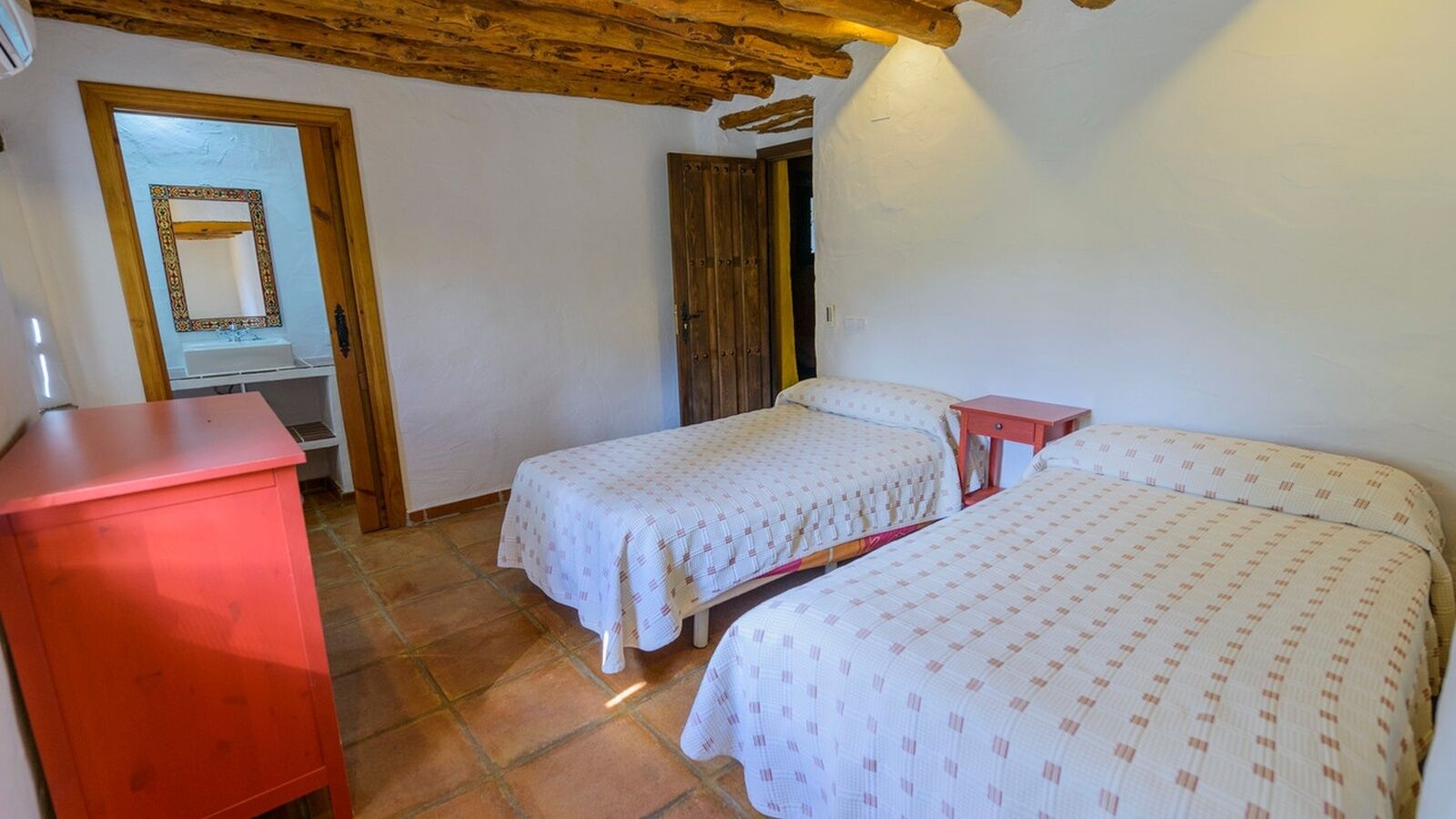 A bedroom with two beds, a wooden wardrobe, a mirror, and a door.
