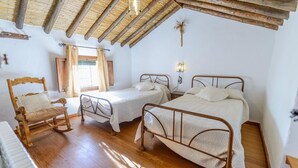 A rustic room with two metal beds, a wooden rocking chair, and a small table.