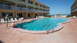 A swimming pool with a tiled deck, a lifeguard stand, and a view of the ocean. - Win San A-208 2BD - Sandy Toes & Salty Breezes (New Smyrna Beach)