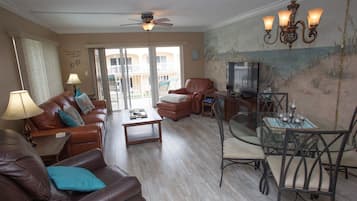 A living room with a brown leather sofa, a glass coffee table, a leather armchair, and a dining area with a glass table and metal chairs.