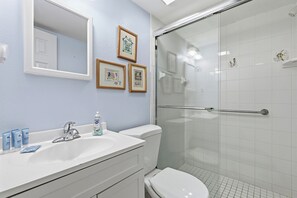 Un bagno con un lavandino bianco, uno specchio e un water, un box doccia in vetro e tre quadri appesi al muro.