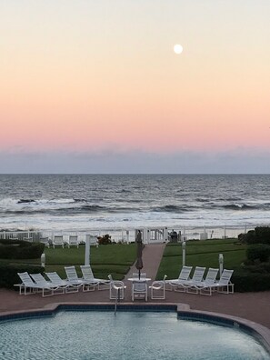 A pool area with lounge chairs and a view of the ocean at sunset.