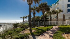 A pathway leading to a beachfront property with palm trees and a white fence. - Win San C-104 2BD - Beach Life Vibes All Day (New Smyrna Beach)