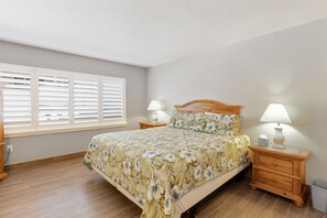 Ein Schlafzimmer mit einem Bett, zwei Nachttischen, einer Nachttischlampe und einem Fenster mit Jalousien.
