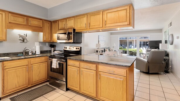 A modern kitchen with wooden cabinets, stainless steel appliances, and a large island. - Win San C-104 2BD - Beach Life Vibes All Day (New Smyrna Beach)