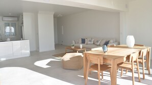 Un vaste espace de vie comprenant une table à manger en bois, un ensemble de canapés et un coin cuisine doté de meubles blancs.