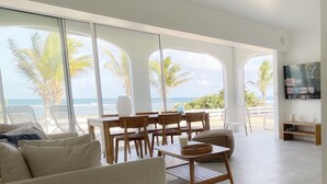 Un vaste espace de vie doté d’une grande fenêtre donnant sur l’océan, et aménagé avec un canapé, une table à manger et des chaises.