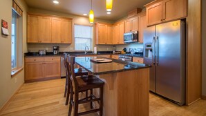 A modern kitchen with wooden cabinets, a stainless steel refrigerator, and a central island with bar stools.