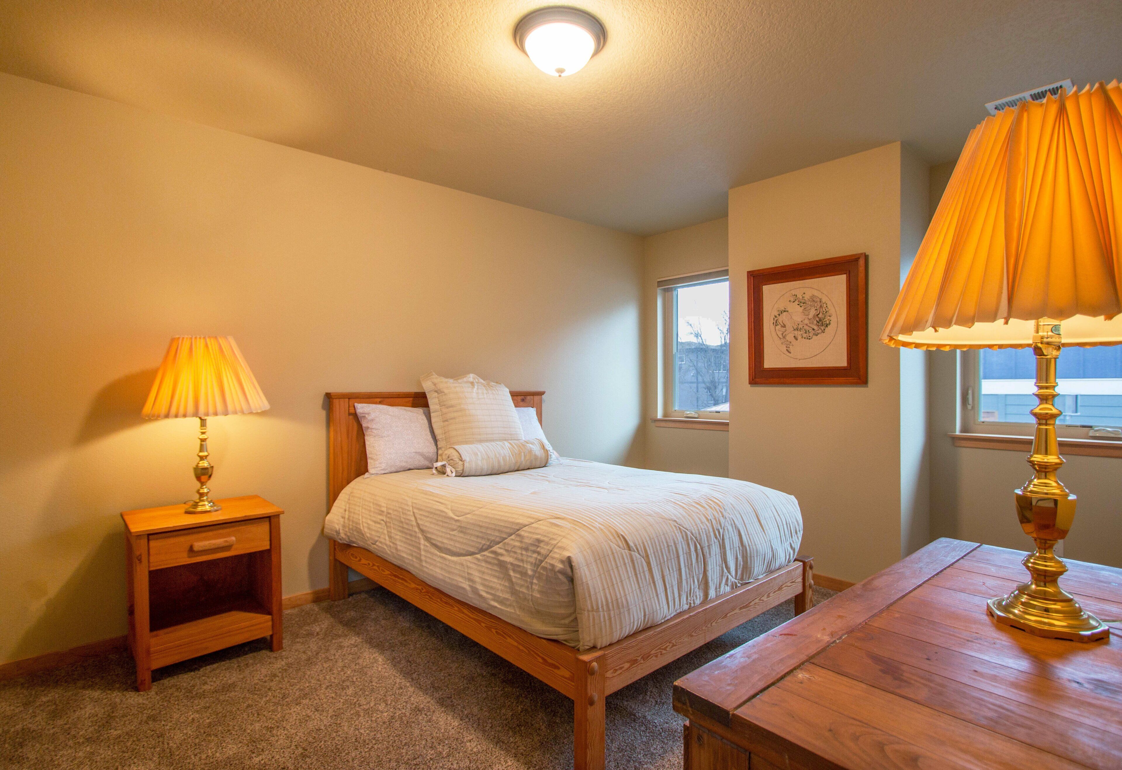 A bedroom with a bed, two bedside tables, a wooden nightstand, a wooden table, and a window with a view.